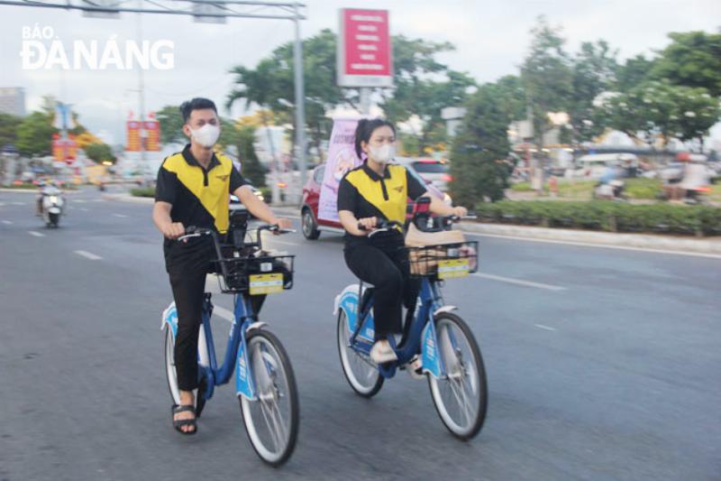 Một chiếc ô tô điện đang được sạc tại trạm sạc, phía sau là cảnh quan đô thị xanh sạch đẹp, thể hiện sự thân thiện với môi trường